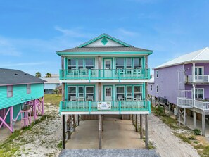 A two-story house with a balcony on the second floor, a small porch on the first floor, and a clear sky in the background. - Twin Palms - Unit 1 - 2 Bedroom • 2 Bath - Private Pool - 150 Feet to the Beach (Gulf Shores)