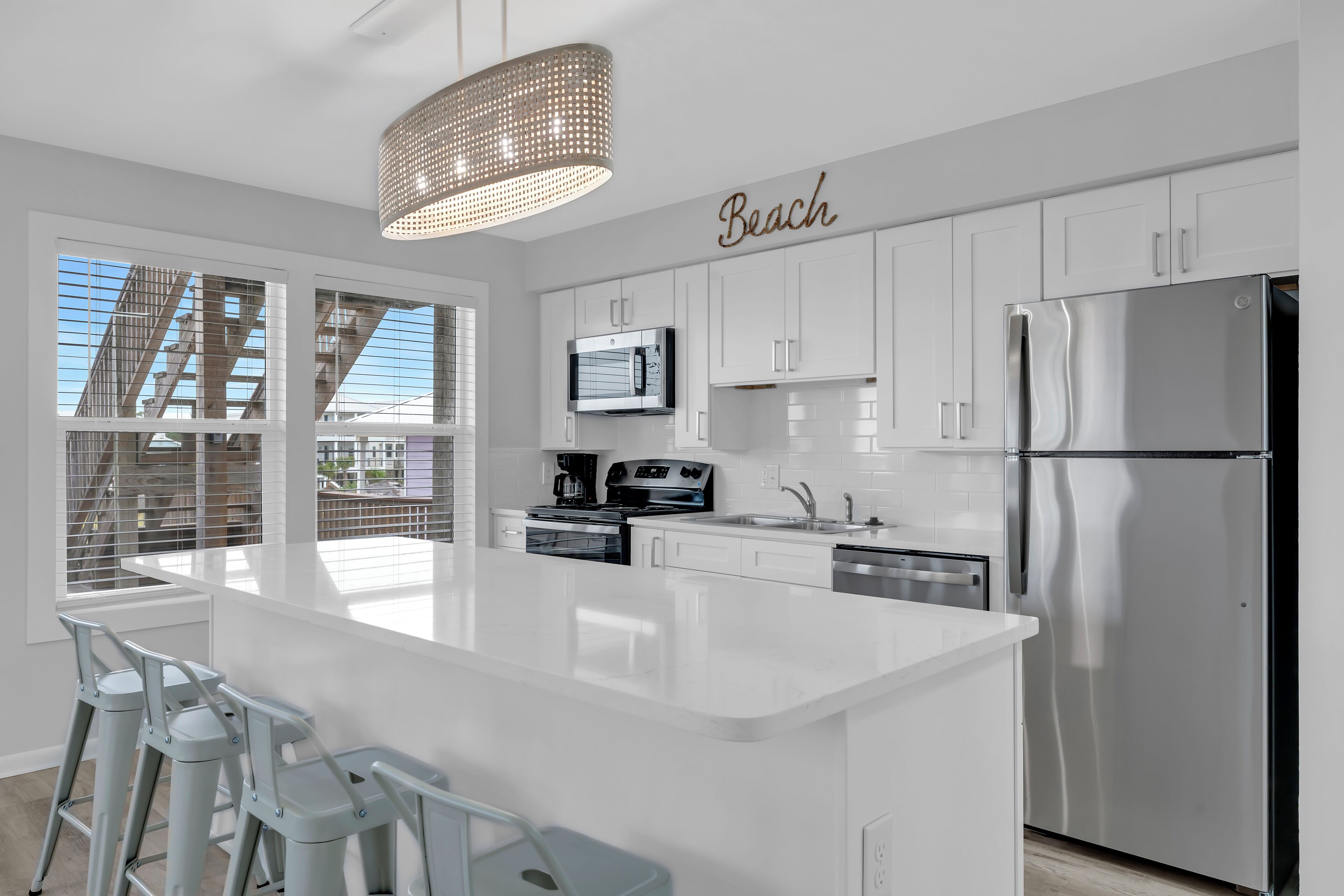 A modern kitchen with white cabinetry, a stainless steel refrigerator, and a large island with bar stools.