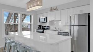 A modern kitchen with white cabinetry, a stainless steel refrigerator, and a large island with bar stools. - Twin Palms - Unit 1 - 2 Bedroom • 2 Bath - Private Pool - 150 Feet to the Beach (Gulf Shores)