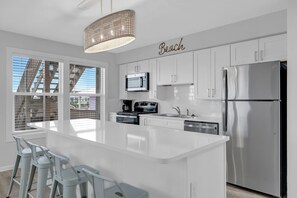 A modern kitchen with white cabinetry, a stainless steel refrigerator, and a large island with bar stools. - Twin Palms - Unit 1 - 2 Bedroom • 2 Bath - Private Pool - 150 Feet to the Beach (Gulf Shores)