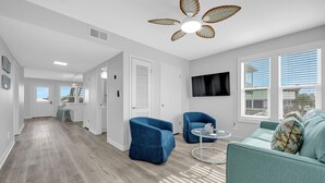A modern living room with a ceiling fan, a flat-screen TV, and a large window with blinds. - Twin Palms - Unit 1 - 2 Bedroom • 2 Bath - Private Pool - 150 Feet to the Beach (Gulf Shores)