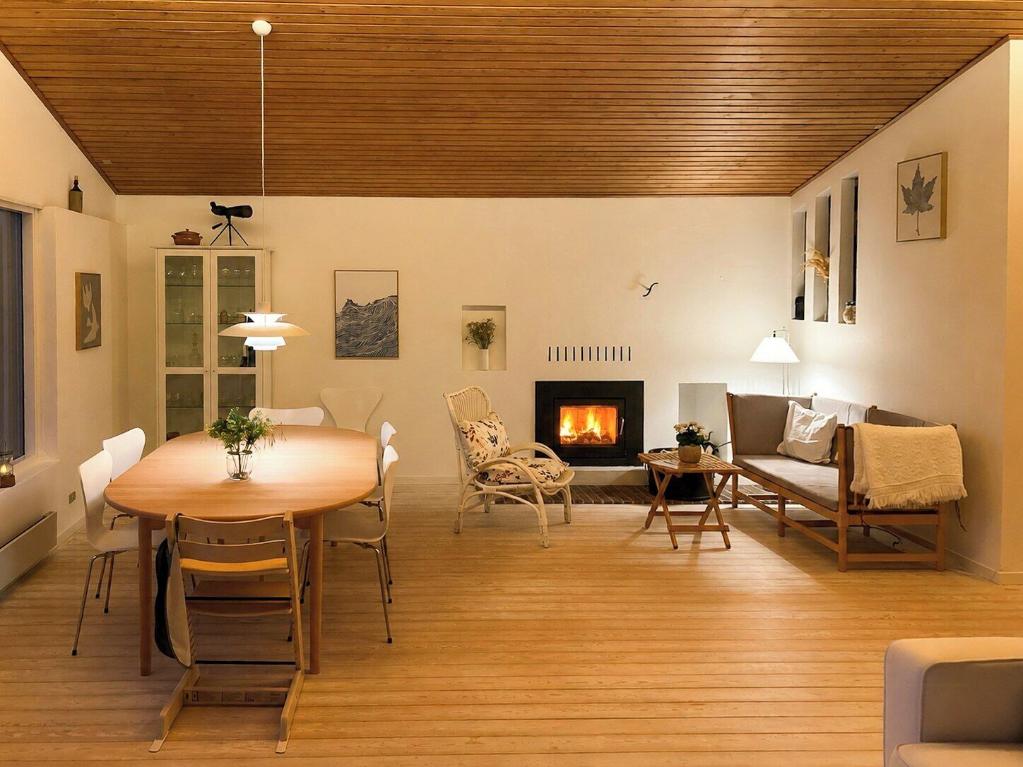 Un salon avec un plancher en bois, une cheminée, une table à manger avec des chaises, un canapé et une lampe.