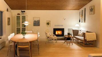 Un salon avec un plancher en bois, une cheminée, une table à manger avec des chaises, un canapé et une lampe.