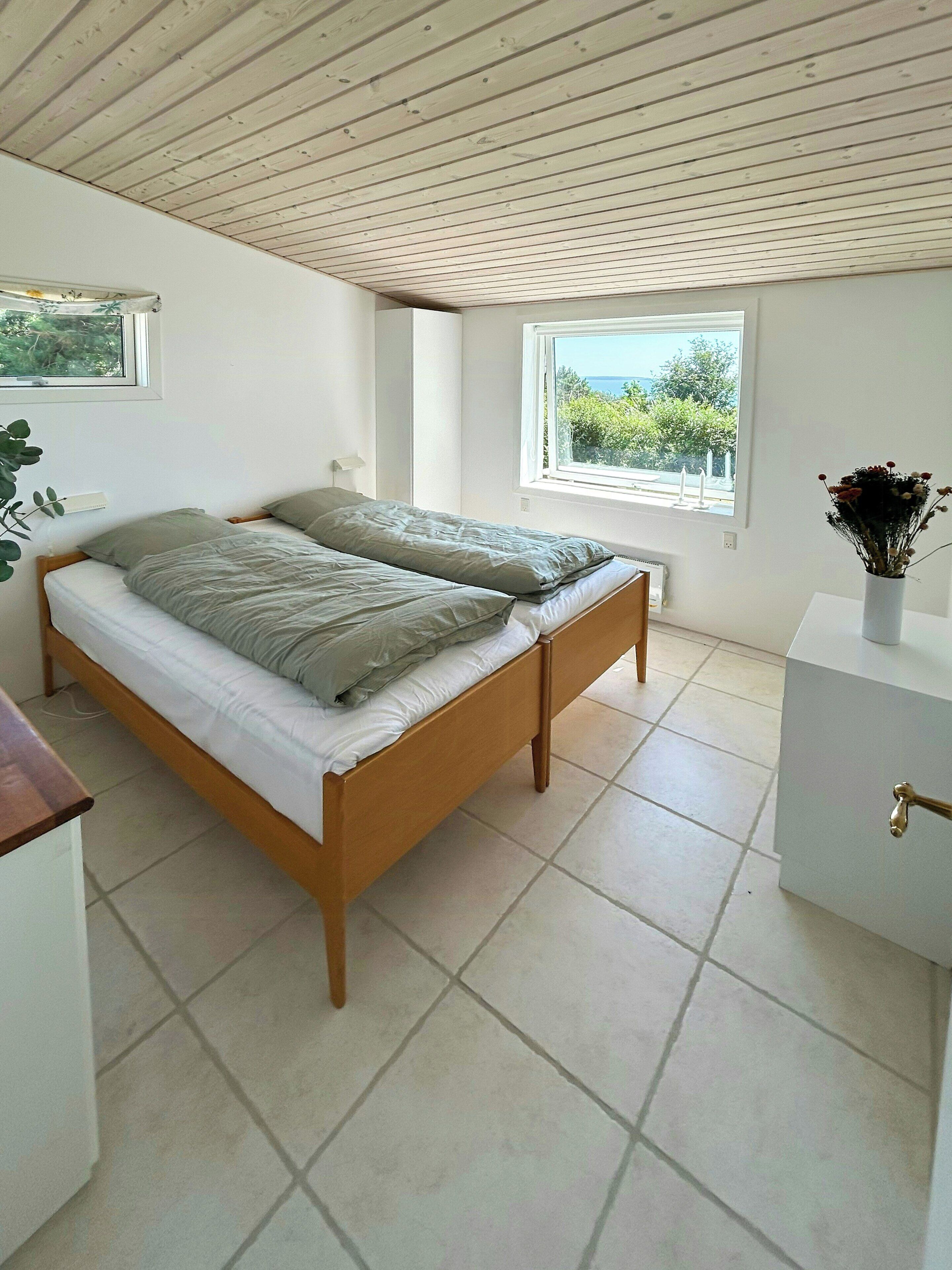A bedroom with a wooden bed, a window with a view, and a bedside table.