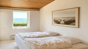Ein Schlafzimmer mit zwei Betten, einer Holzbalkendecke, einem Fenster mit Blick und einem gerahmten Bild an der Wand.
