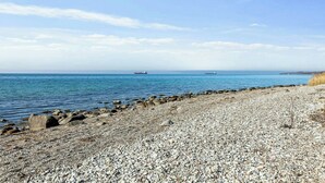 Ein Kiesstrand mit ruhiger See und Schiffen am Horizont.
