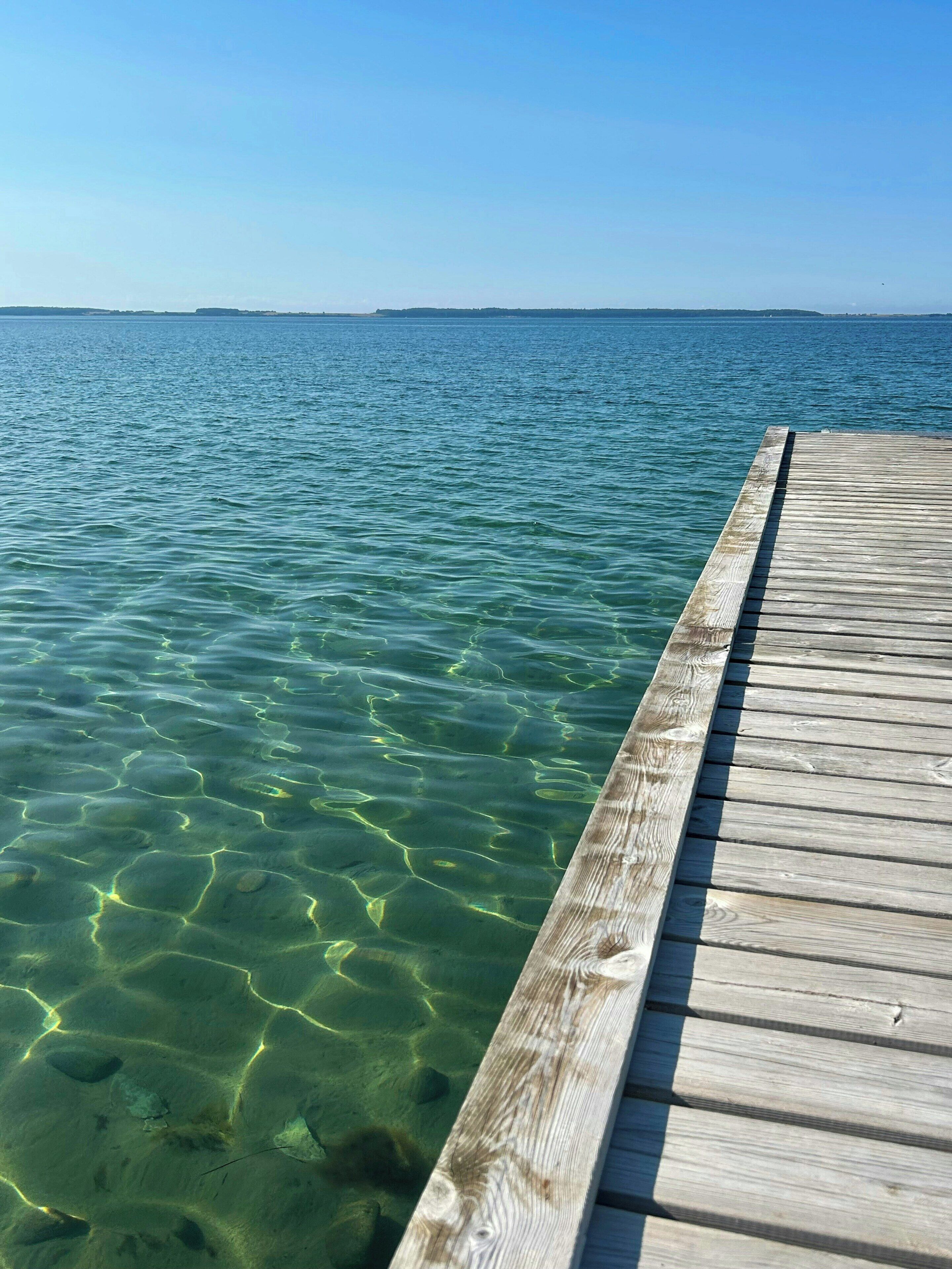 Une jetée en bois s’étendant dans une eau d’un bleu limpide, où l’on peut distinguer des motifs sous-marins.