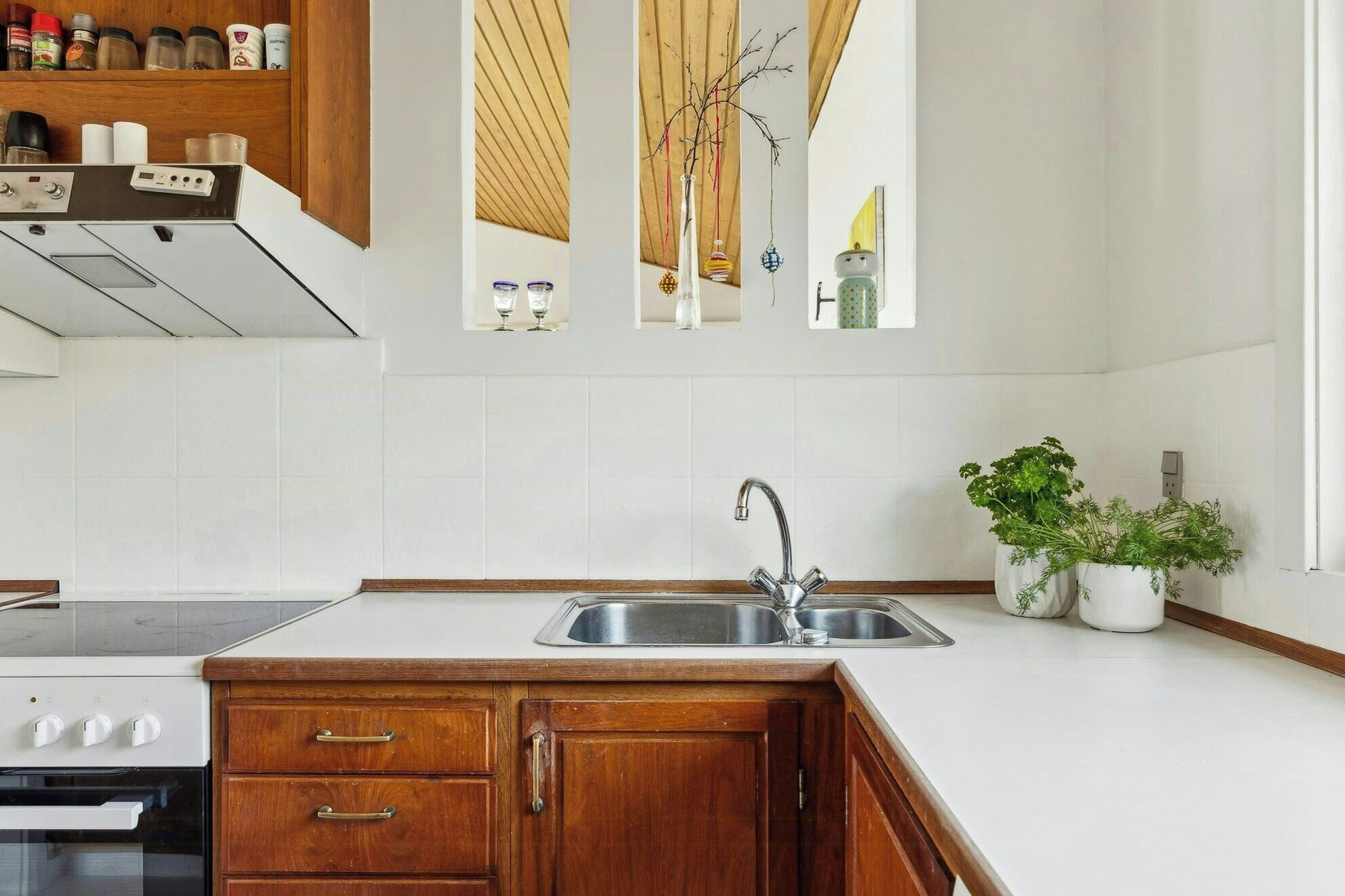 Una cucina con un lavello a due vasche, mobili in legno, un fornello e una dispensa con spezie.