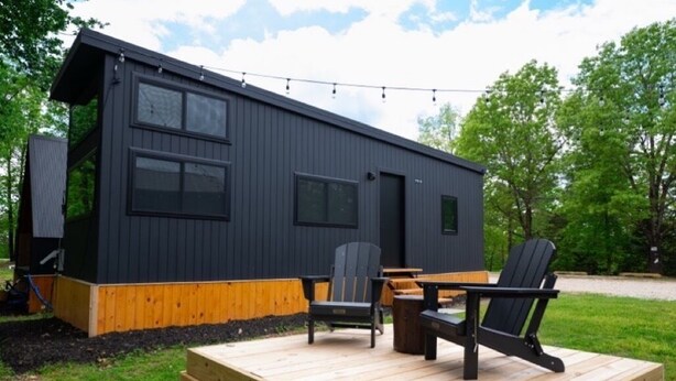 Una cabaña moderna con terraza, asientos al aire libre y luces decorativas.
