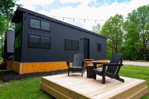 A modern cabin with a deck, outdoor seating, and a string of lights. - NWA Peaceful Pine Cabin at Beaver Lake (Rogers)