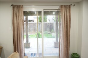 Une pièce dotée d’une porte-fenêtre coulissante donnant sur un patio, d’une poubelle verte et d’une chaise beige.