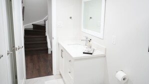 Ein Badezimmer mit einem weißen Waschbecken, einem Spiegel und einer dunklen Holztreppe, die in ein weiteres Zimmer führt.