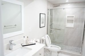 Un baño moderno con ducha acristalada, un lavabo blanco con espejo y un inodoro con tapa blanca.