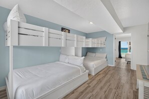 Ein Schlafzimmer mit zwei Betten, einem Deckenventilator und Meerblick durch eine offene Tür.