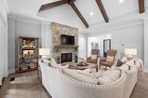 A living room with a stone fireplace, wooden beams, a sofa set, and a bookshelf. - McLemore Resort - 18 Hawthorne Lane - Golf Course View (Rising Fawn)