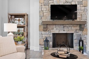 A living room with a stone fireplace, a mounted TV, a bookshelf, and a comfortable sofa. - McLemore Resort - 18 Hawthorne Lane - Golf Course View (Rising Fawn)