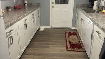 Une cuisine avec des meubles blancs, des plans de travail en granit, un tapis rouge et une porte avec une fenêtre.