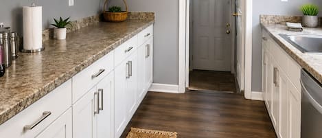 Una cocina con armarios blancos, encimeras de granito y piso de madera.