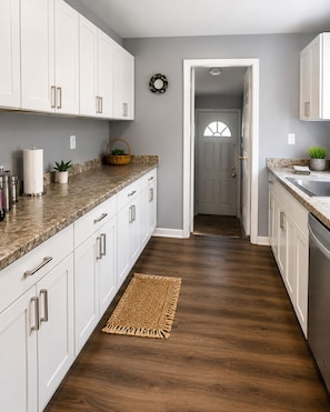Una cocina con armarios blancos, encimeras de granito y piso de madera.