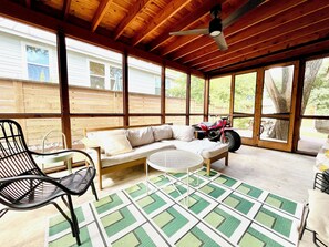 A covered patio with a wooden ceiling, a sofa, a chair, a small table, and a red ATV. - Serene, charming 2-bed bungalow, filled with art and light, in Central Austin (Austin)