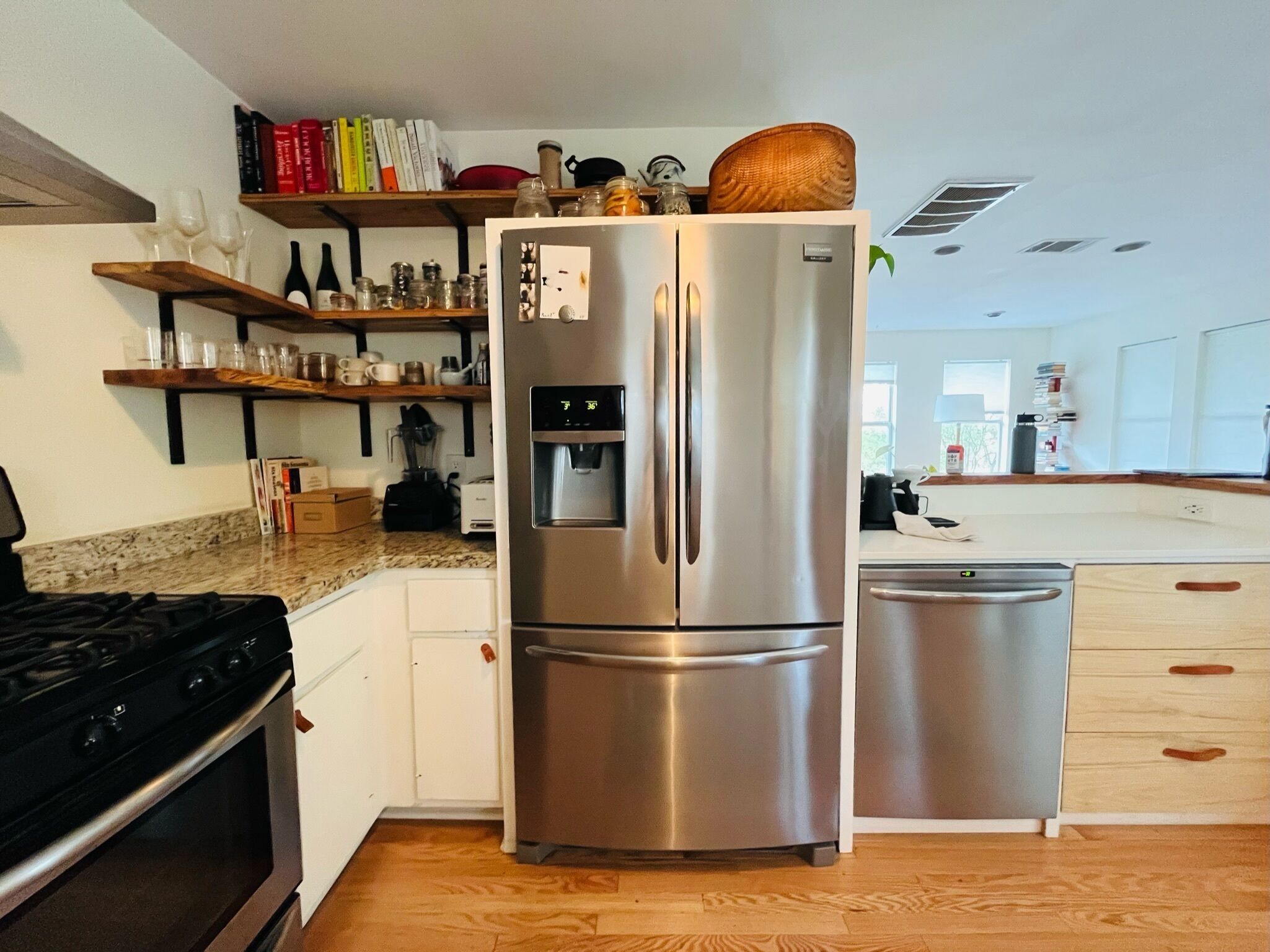 Une cuisine moderne dotée d’appareils électroménagers en acier inoxydable, d’étagères en bois et d’un distributeur d’eau intégré.