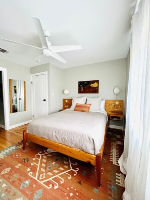 A bedroom with a bed, a ceiling fan, a nightstand, a lamp, and a rug. - Serene, charming 2-bed bungalow, filled with art and light, in Central Austin (Austin)