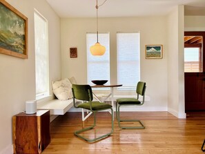 A modern dining area with a wooden table, two green chairs, a white bench with cushions, and a hanging pendant light. - Serene, charming 2-bed bungalow, filled with art and light, in Central Austin (Austin)