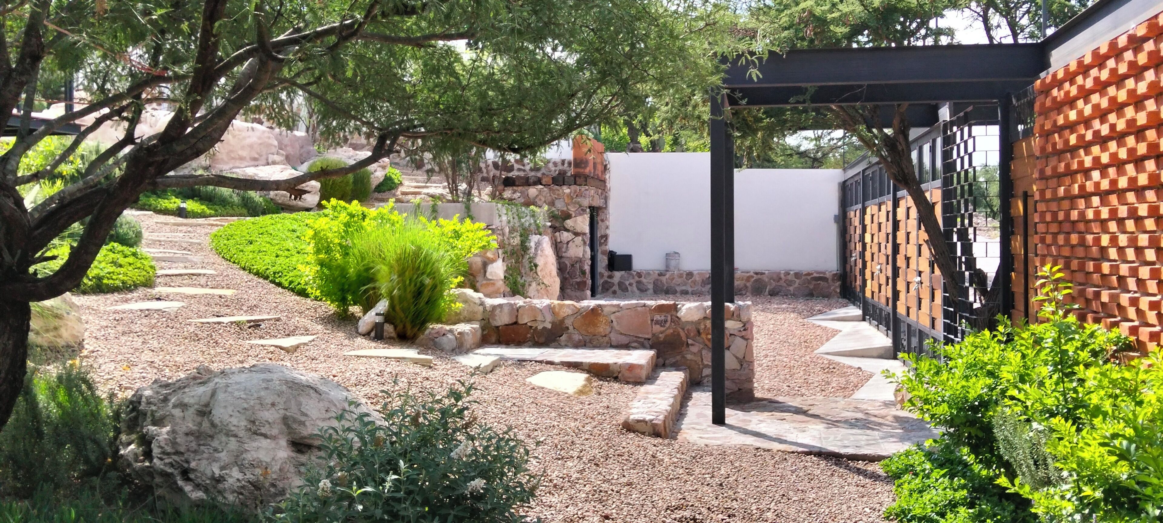 Un jardin avec un chemin de pierre, une pergola et un mur en briques.