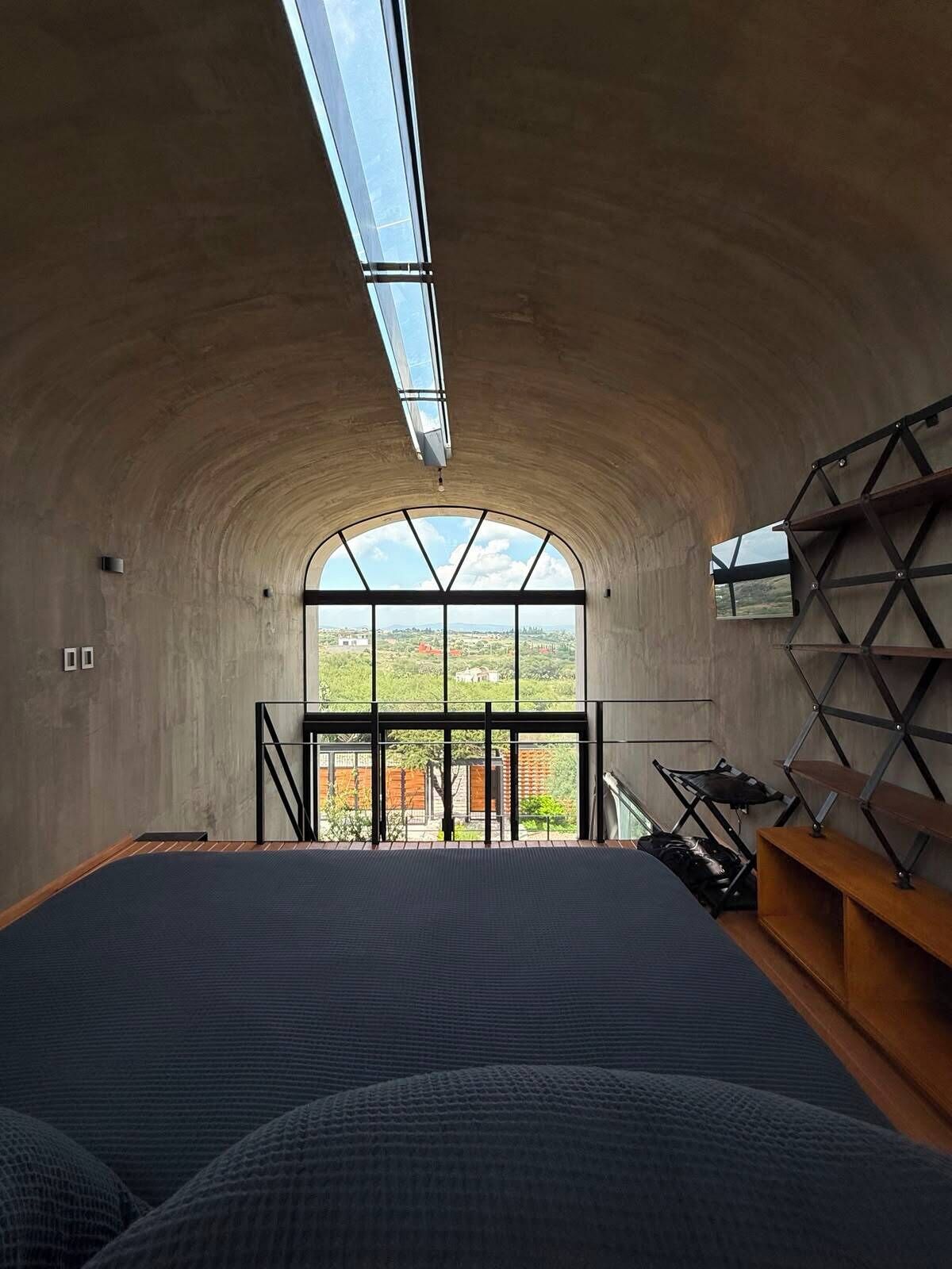 A room with a large arched window, a bed, and a wooden shelf unit.