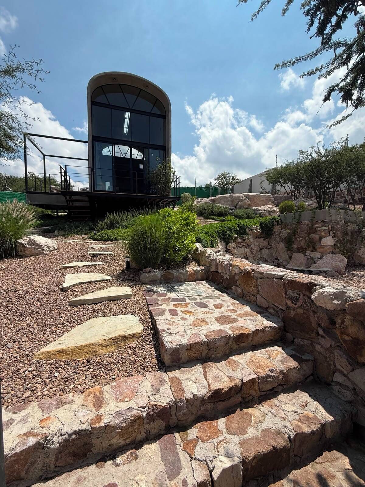 A modern building with a curved glass facade, surrounded by a landscaped garden with a stone pathway.