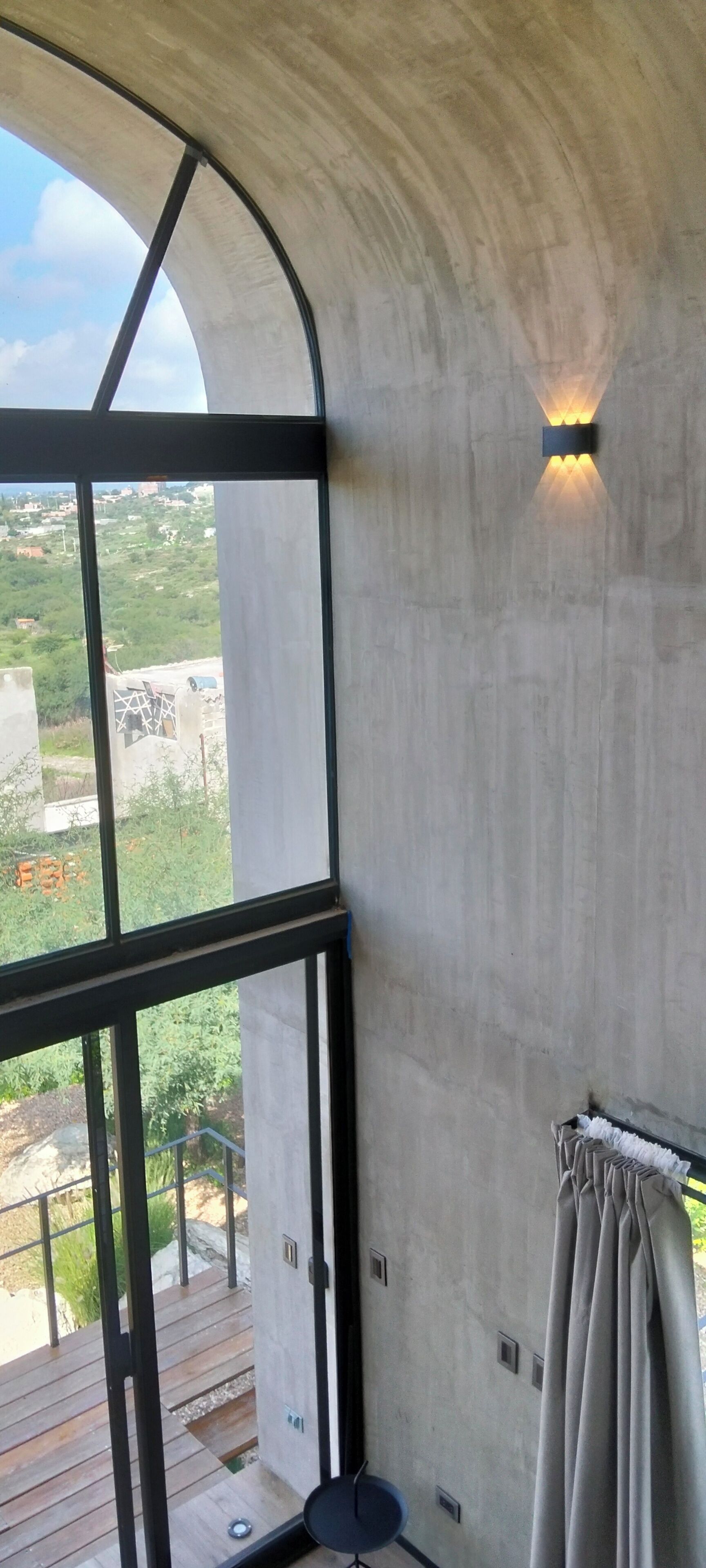 Une pièce dotée d’une grande fenêtre, d’un mur en béton et offrant une vue sur le paysage.