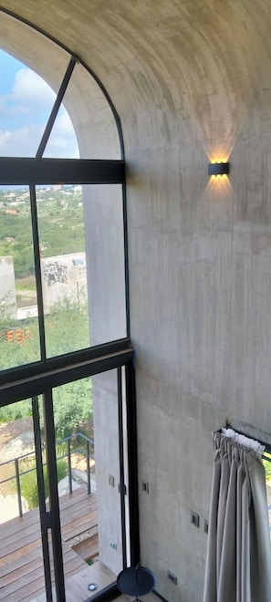 Een kamer met een groot raam, een betonnen muur en uitzicht op het landschap.
