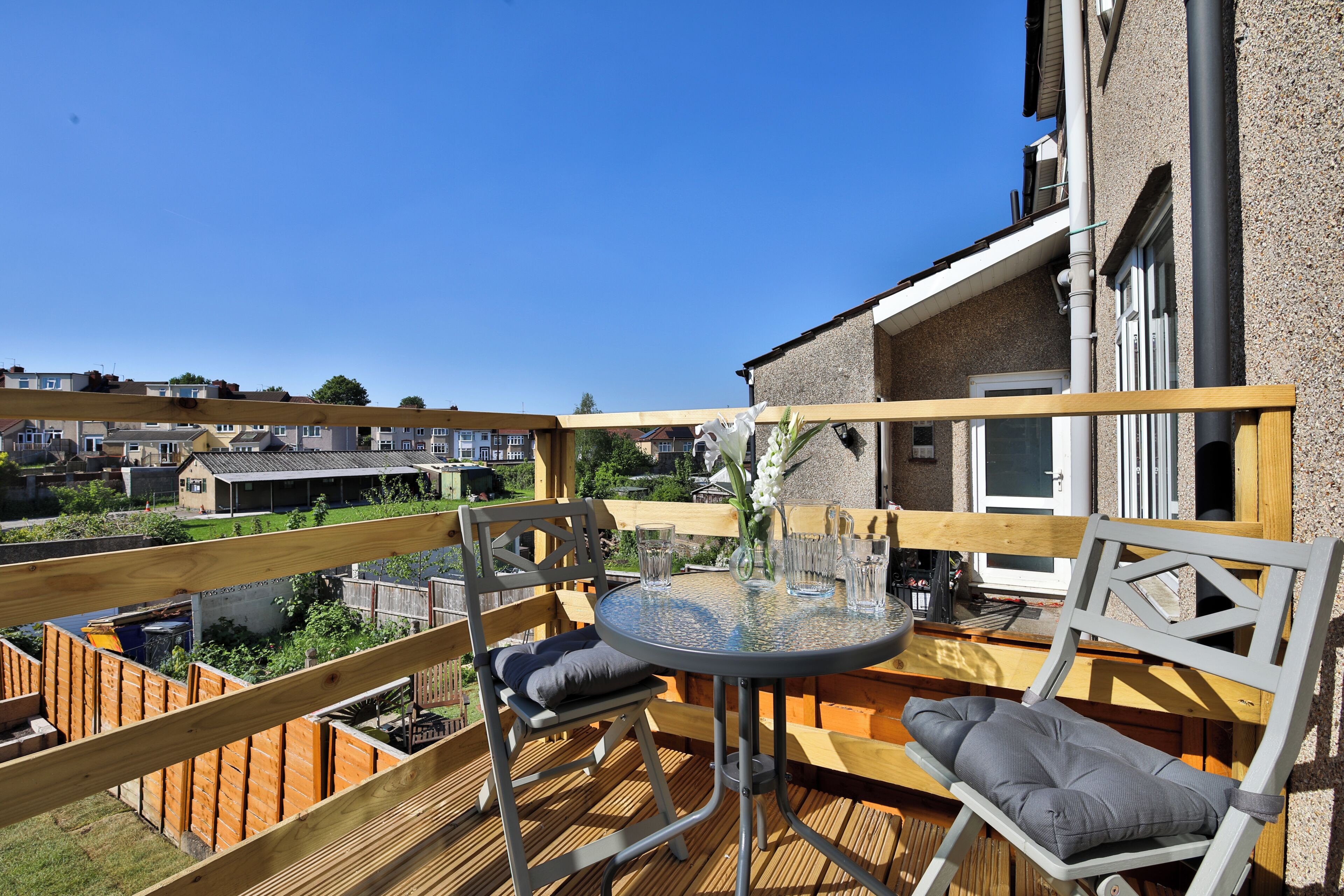 A wooden deck with a round table and two chairs, overlooking a residential area.