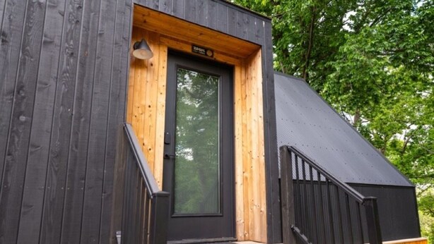 A wooden cabin with a black door, a small porch, and a black staircase. - A-Frame Retreat at Beaver Lake - Sleeps 4 near Rogers & Bentonville (Rogers)