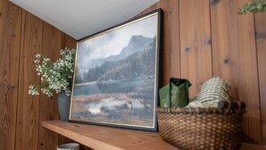 A framed landscape painting on a wooden shelf, a woven basket, and a vase with white flowers. - A-Frame Retreat at Beaver Lake - Sleeps 4 near Rogers & Bentonville (Rogers)