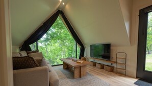 A modern living room with a large window, a sofa, a coffee table, and a flat-screen TV. - A-Frame Retreat at Beaver Lake - Sleeps 4 near Rogers & Bentonville (Rogers)
