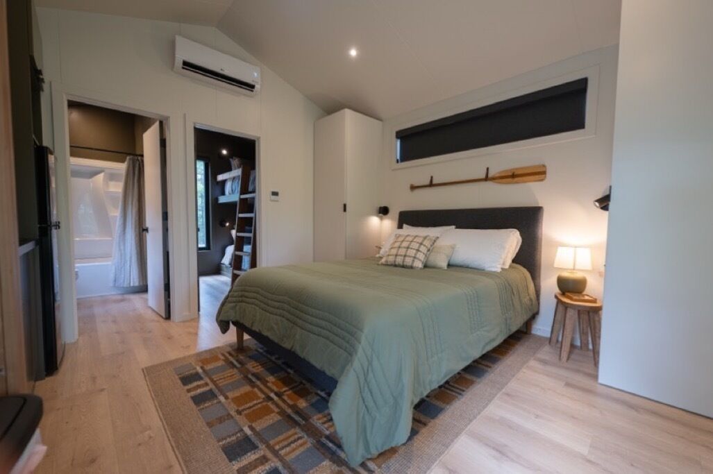 Un dormitorio con cama, lámpara de mesita de noche, estante en la pared y ventana.