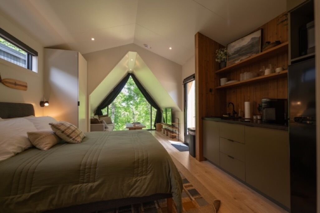 Un dormitorio con una cama grande, vistas por la ventana y una kitchenette con armarios de madera.