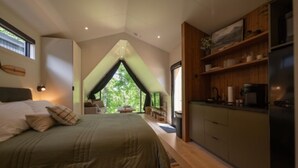 A bedroom with a large bed, a view through a window, and a kitchenette with wooden cabinets. - A-Frame Retreat at Beaver Lake - Sleeps 4 near Rogers & Bentonville (Rogers)