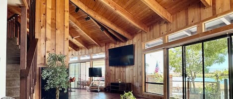 A spacious living area with a high ceiling, wooden beams, a round coffee table, a sofa, and a television.