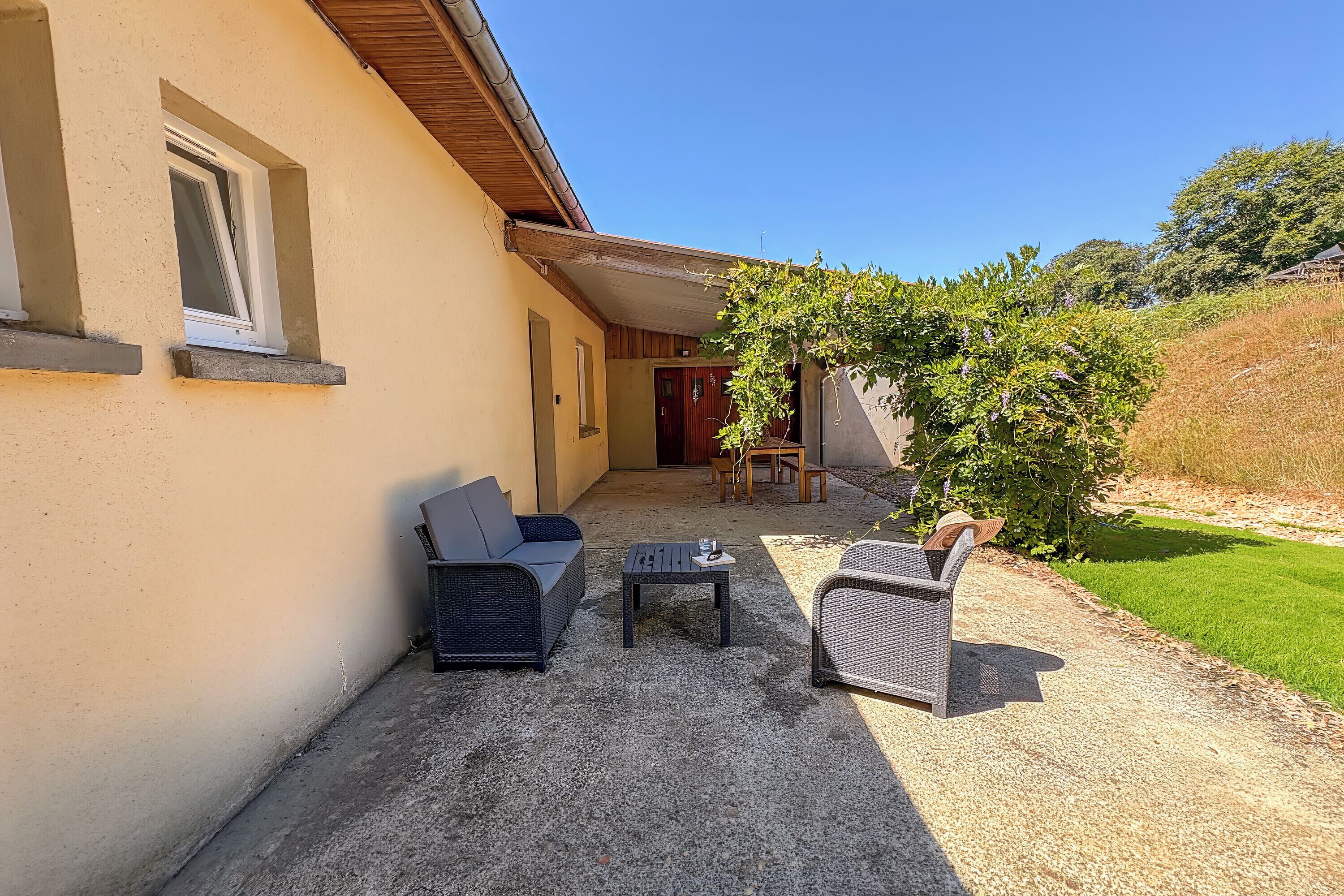 Eine Terrasse mit Gartenmöbeln, einem kleinen Tisch und einer Tür zu einem Innenraum.