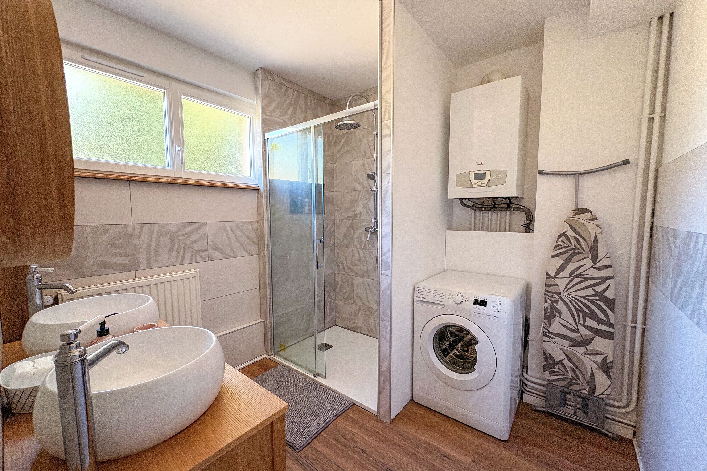 A bathroom with a glass-enclosed shower, a washing machine, and two sinks.