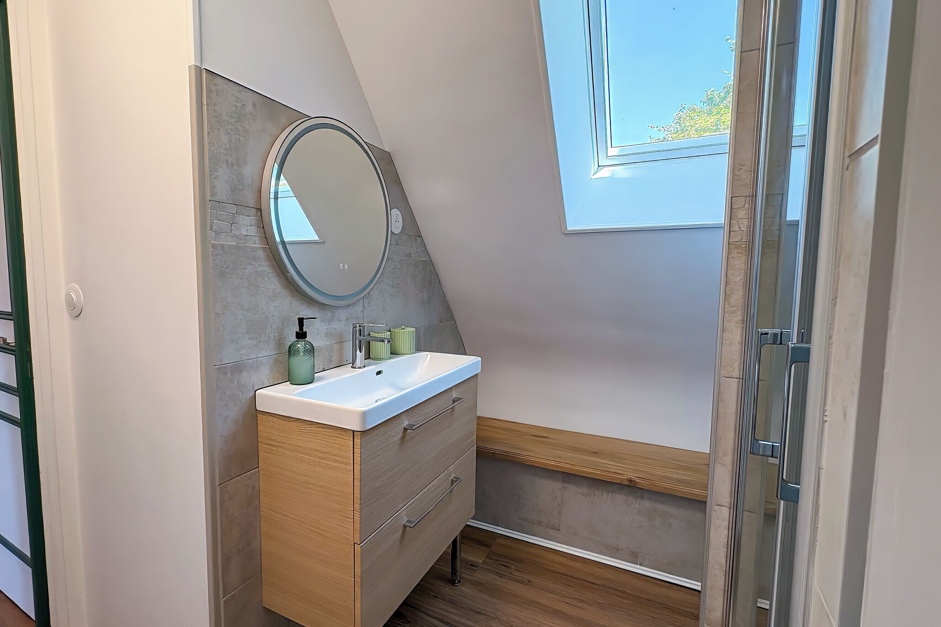 Un baño moderno con tocador, espejo redondo y ventana.