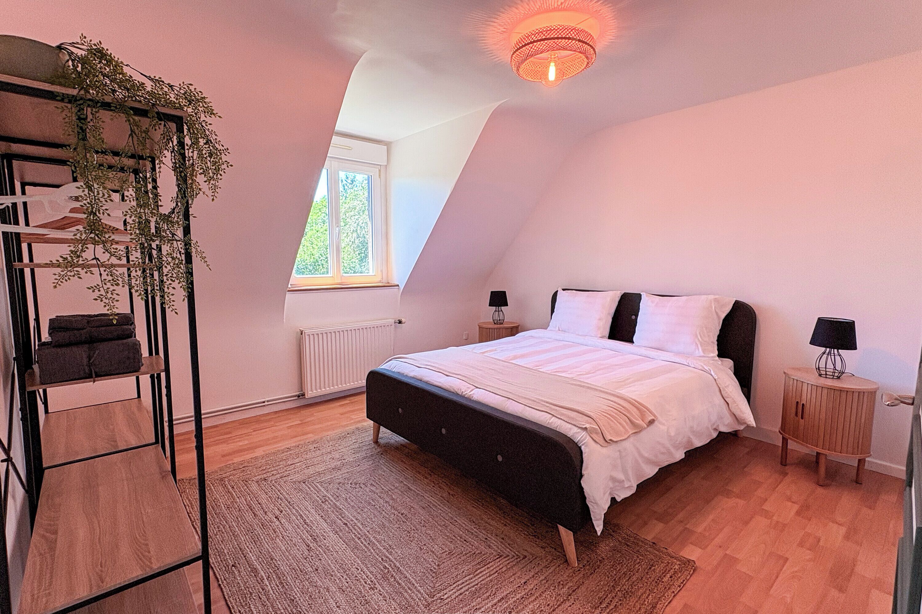 A bedroom with a bed, a radiator, a window, a plant, and a lamp.