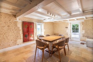 A dining area with a wooden table and chairs, a red cabinet with floral designs, and a view through a glass door. - La Courberie - Piscine - Petfriendly (Villetoureix)