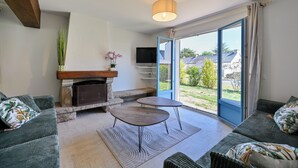 Una sala de estar con chimenea, televisor y un amplio ventanal corredera que da a un jardín.