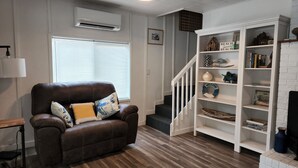 Una sala de estar con un sofá de cuero marrón, una estantería blanca y una escalera.