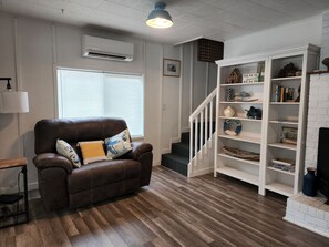 Ein Wohnzimmer mit braunem Ledersofa, einem weißen Bücherregal und einer Treppe.