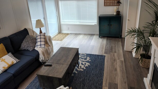 Sala de estar con sofá, mesa de centro y aparador. Hay ventanas con persianas, una lámpara y una planta.
