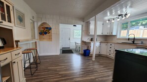Una cocina con suelo de madera, armarios blancos, lavavajillas negro y una ventana con vista al exterior.